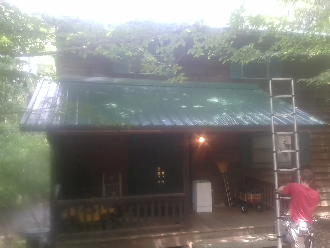 Worker on a ladder at the green porch roof of a wooded cabin in Round Lake