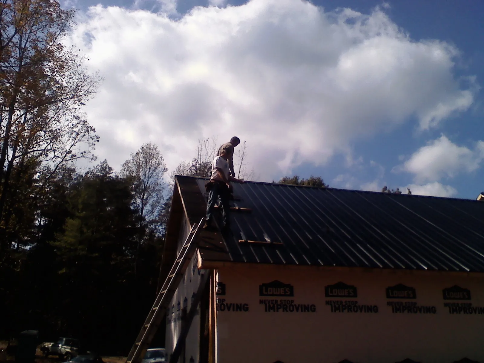 Roofer fastening dark metal panels high against a cloudy sky, from a Roof Inspection job in Round Lake