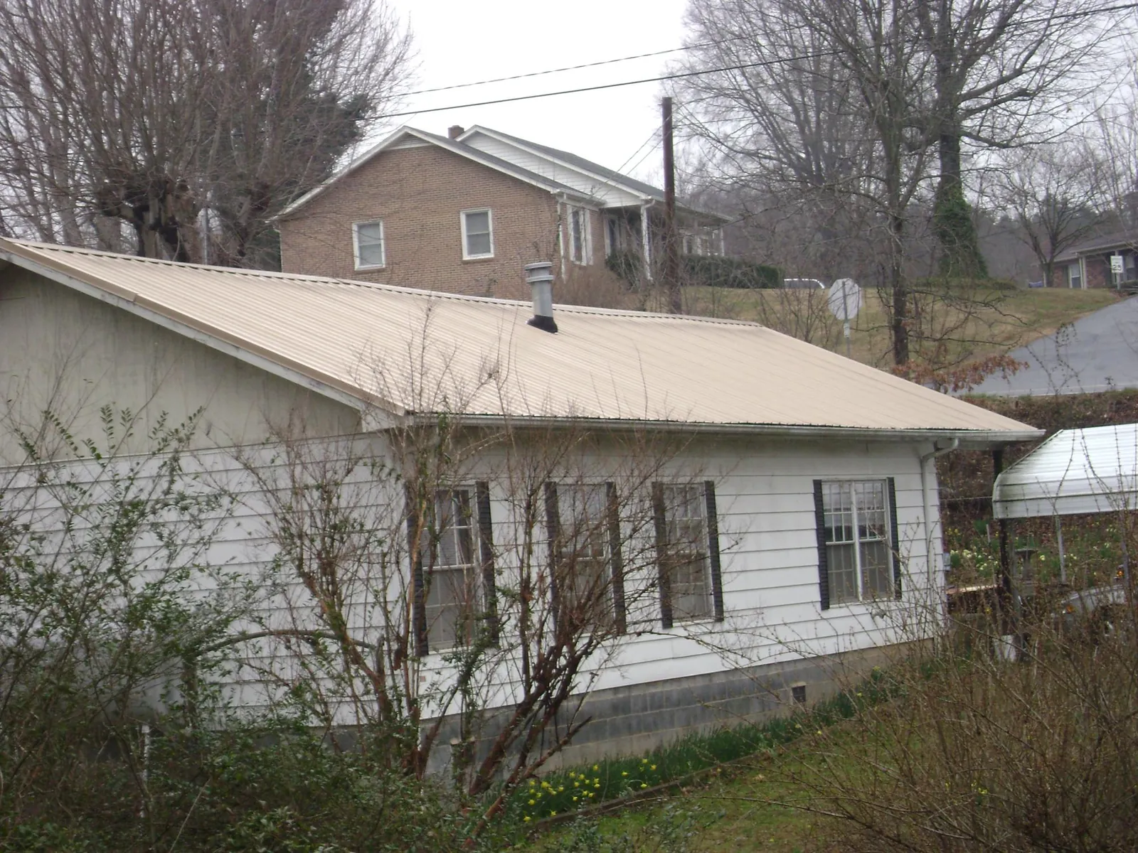 Tan metal roof on a white sided house set into a hillside — Commercial Roofing by Roofing Brothers in Round Lake